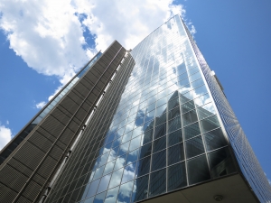 Impressive view from below of a towering glass building with the sky and clouds vividly mirrored across its many windows.